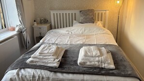 A neatly made bed with white and gray linens, a bedside table with a lamp, and a window with curtains.