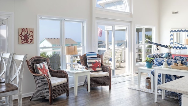 A spacious room with large windows, wicker furniture, and a view of the ocean. - Bluebird By the Sea: Almost Oceanfront with Private Hot Tub! (Emerald Isle)