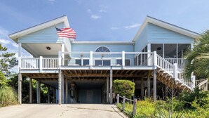 A two-story house with a covered front porch, a flag, and a staircase leading to a second level. - Bluebird By the Sea: Almost Oceanfront with Private Hot Tub! (Emerald Isle)