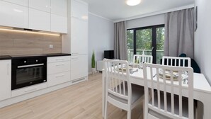 Eine moderne Küche mit weißen Schränken, einem schwarzen Backofen und einem Essbereich mit weißem Tisch und Stühlen.