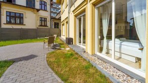 Ein modernes Gebäude mit großen Glasfenstern, einer gepflasterten Terrasse und einer Rasenfläche.