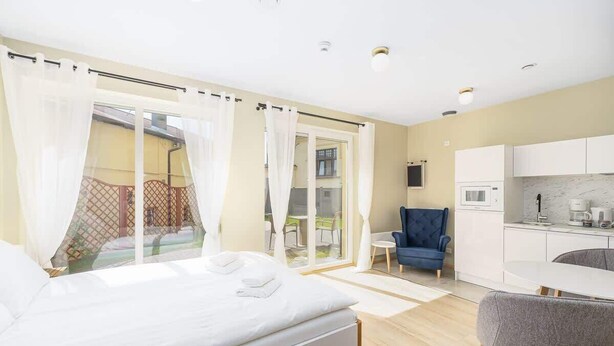 Ein modernes Hotelzimmer mit Bett, kleinem Schreibtisch, Stuhl, einer Küchenzeile und einem Balkon mit Vorhängen.