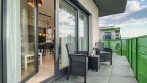 A balcony with wicker furniture, a glass door leading to an interior space, and a green safety fence.