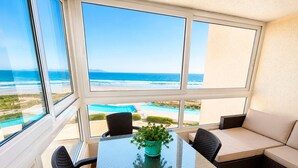 Une pièce avec une table en verre, des chaises, un canapé et une vue sur l’océan et la piscine.