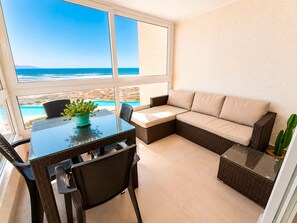 A room with a glass table, a sofa, and a view of the ocean.