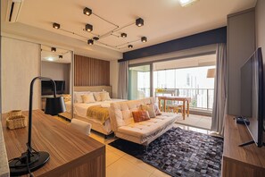 Habitación de hotel moderna con cama, sofá, escritorio y un amplio ventanal con vista a la ciudad.