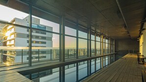 A modern indoor pool area with large windows, wooden flooring, and a view of a cityscape.