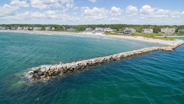 A coastal view with a rocky breakwater extending into the sea, a sandy beach, and houses in the background. - Kennebunk Coastal Getaway ! 2 minutes from Gooch's Beach ! (Kennebunk)