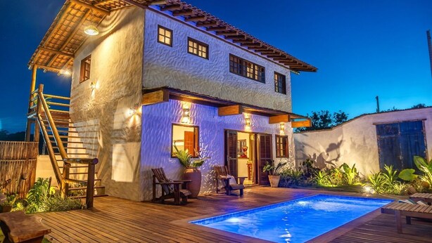Una casa de dos pisos con piscina, terraza de madera y zona de estar al aire libre.