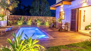 Una piscina con muelle de madera, sillas de descanso y un área de patio techada.