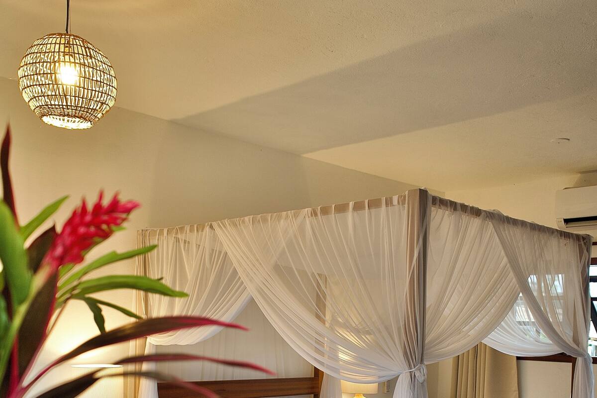 Quarto com cama de dossel, mesas de cabeceira, um banquinho e um banco.