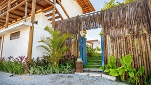 Un edificio tradicional con un balcón de madera, entrada con techo de paja y un jardín bien cuidado con diversas plantas.