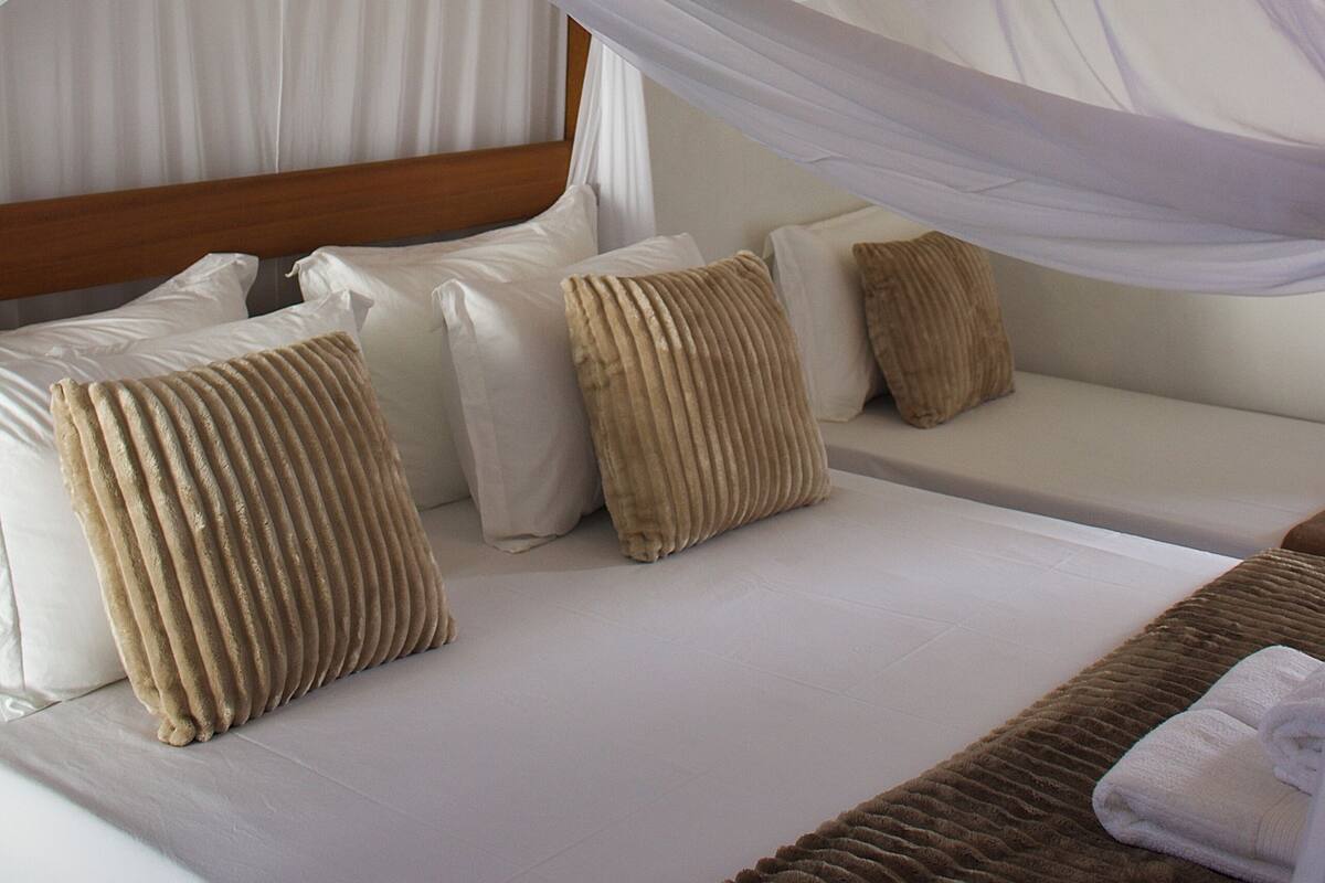 Uma cama com dossel, almofadas e cabeceira.