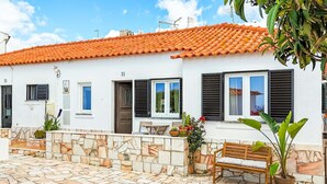 A white building with a tiled roof, numbered 31, featuring a stone wall, a wooden bench, and potted plants. - Casa Bela Mar (Albufeira)
