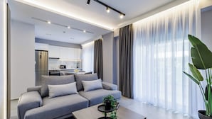 A modern living room with a grey sofa, a coffee table, and a large plant. - The Kokoon Volos Comfort Living (Volos)