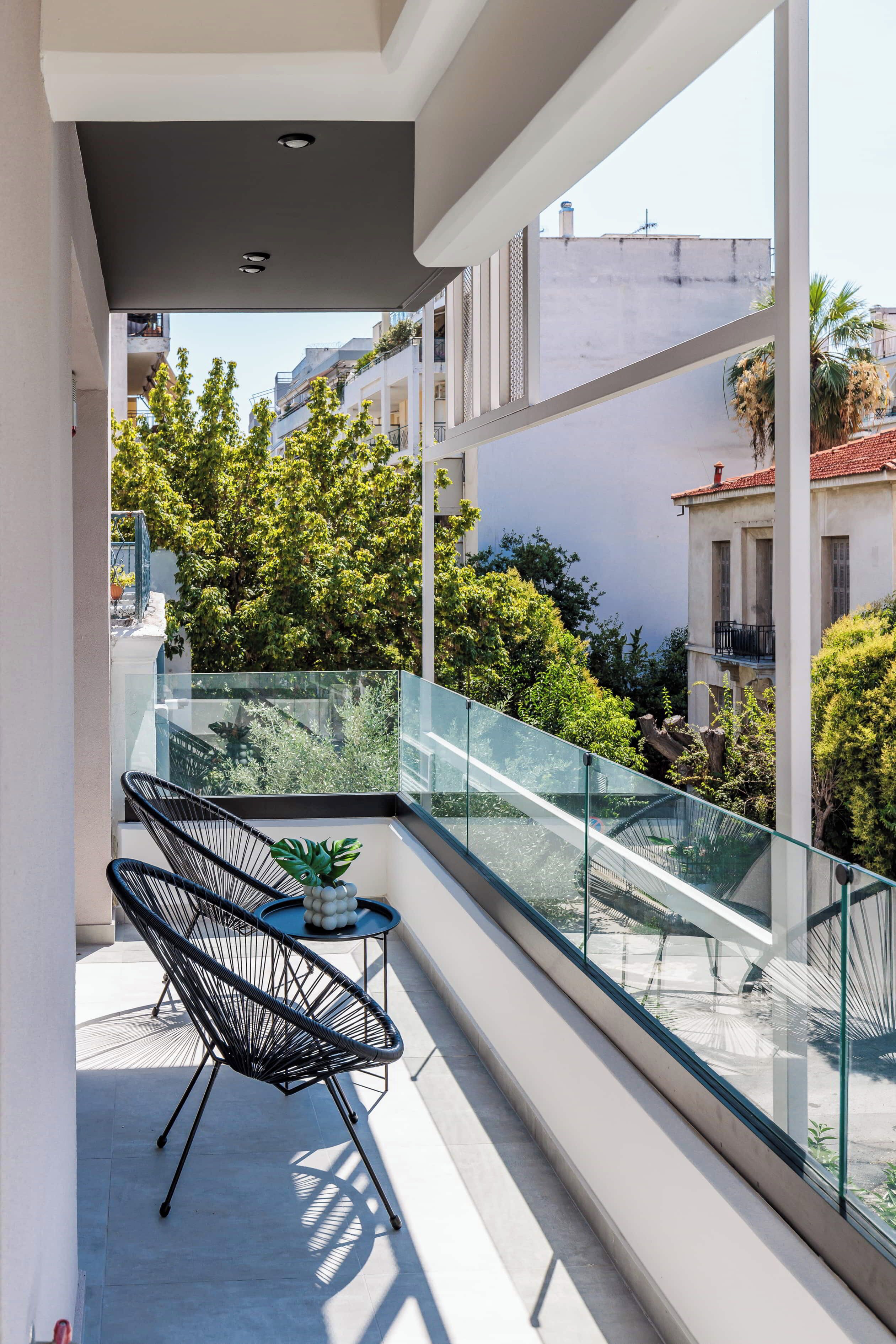 Un balcon doté d’une balustrade en verre, d’une chaise en fil de fer noir et d’une petite table sur laquelle est posée une plante.