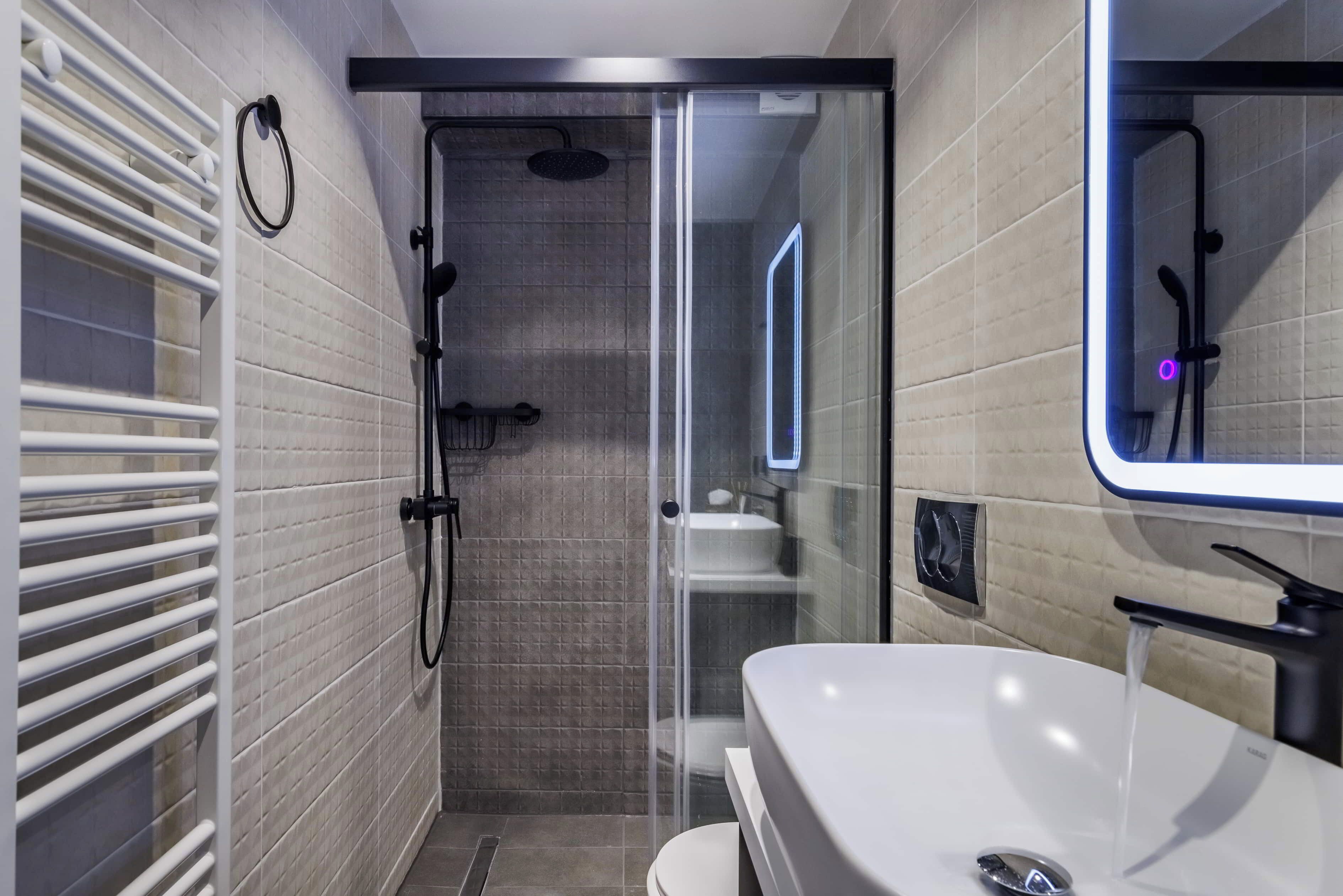 A modern bathroom with a glass-enclosed shower, a white sink, and a towel rack.