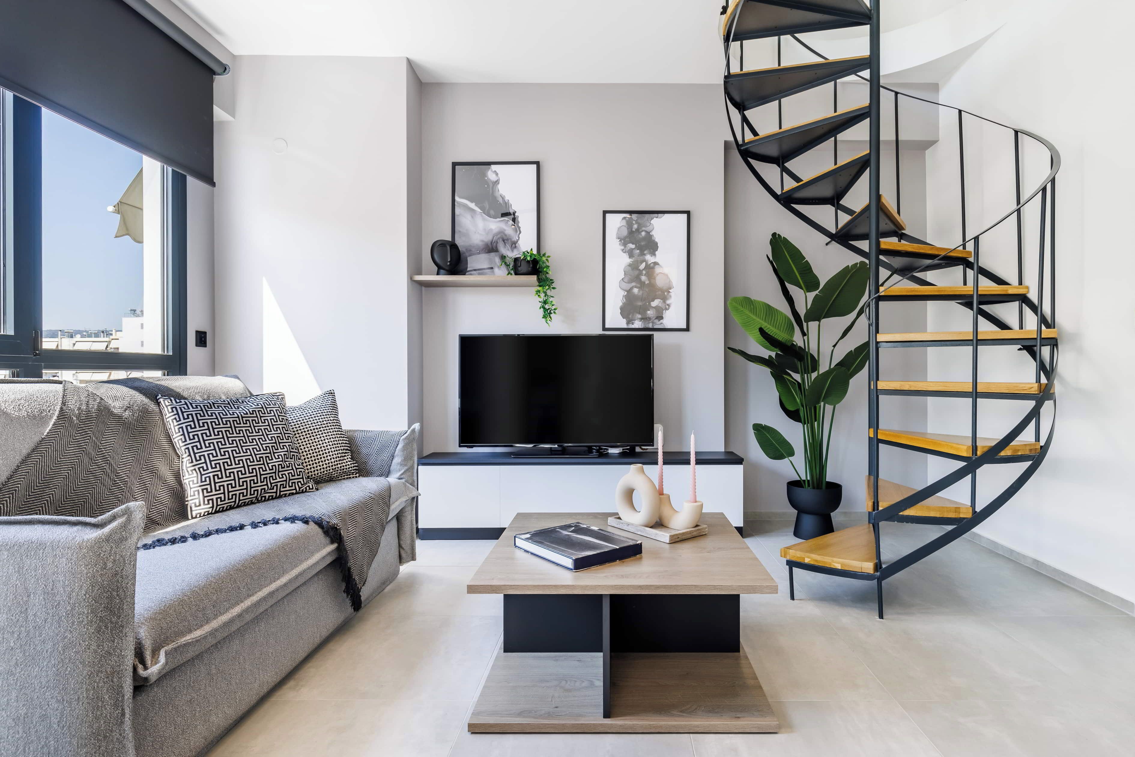 Een moderne woonkamer met een gebogen trap, een bank, een salontafel, een televisie en kunstwerken in lijsten aan de muur.