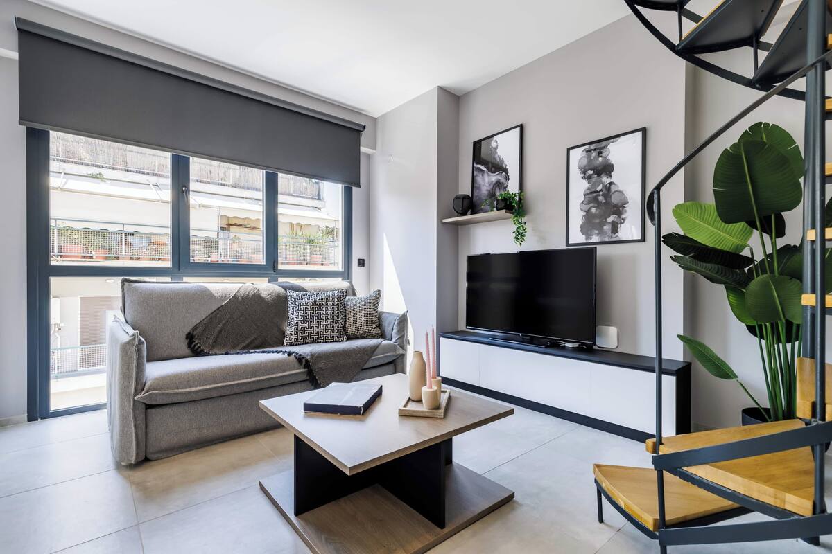 Ett modernt vardagsrum med en soffa, ett soffbord, en tv och en trappa.