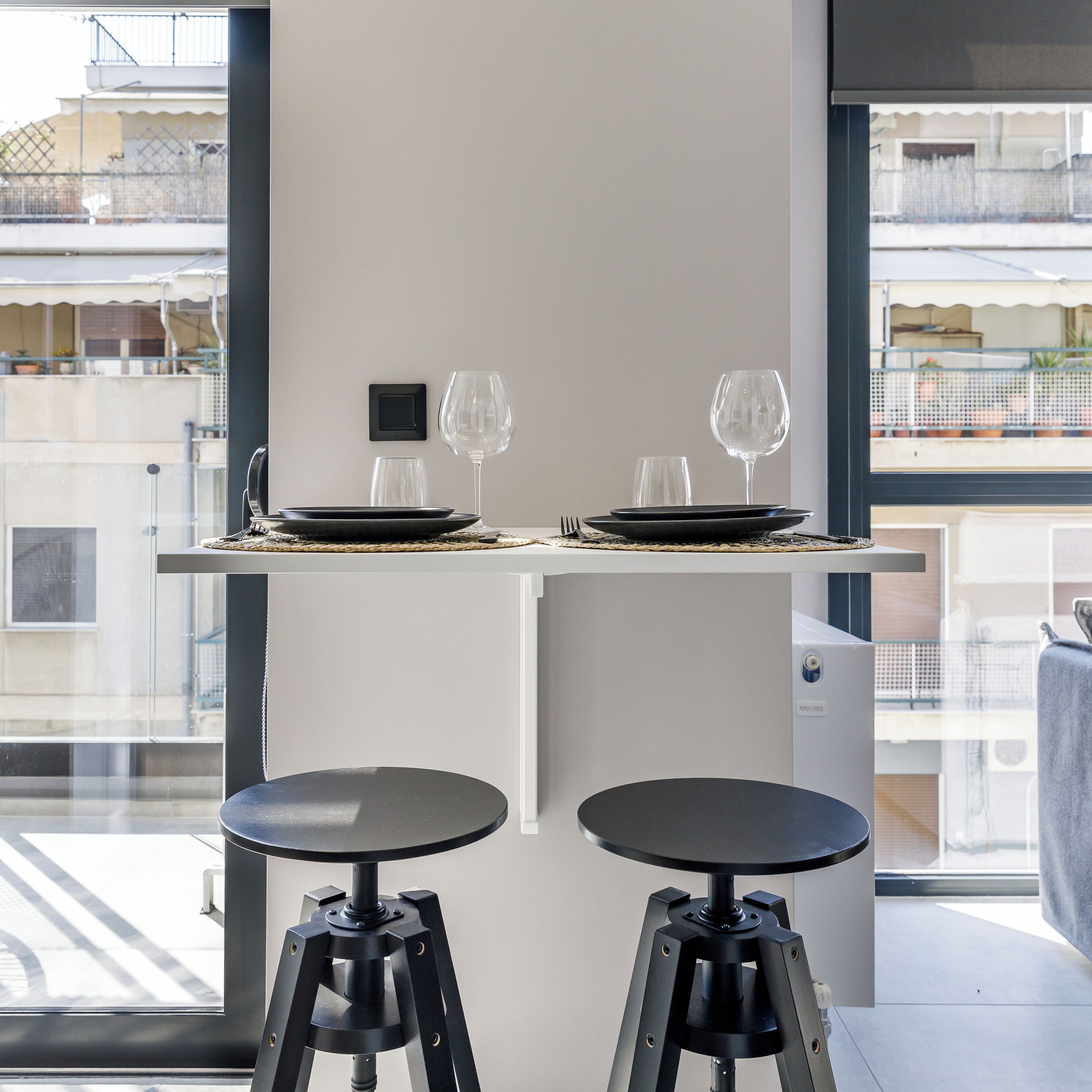 A modern dining area with two black stools, a small table, and two wine glasses.