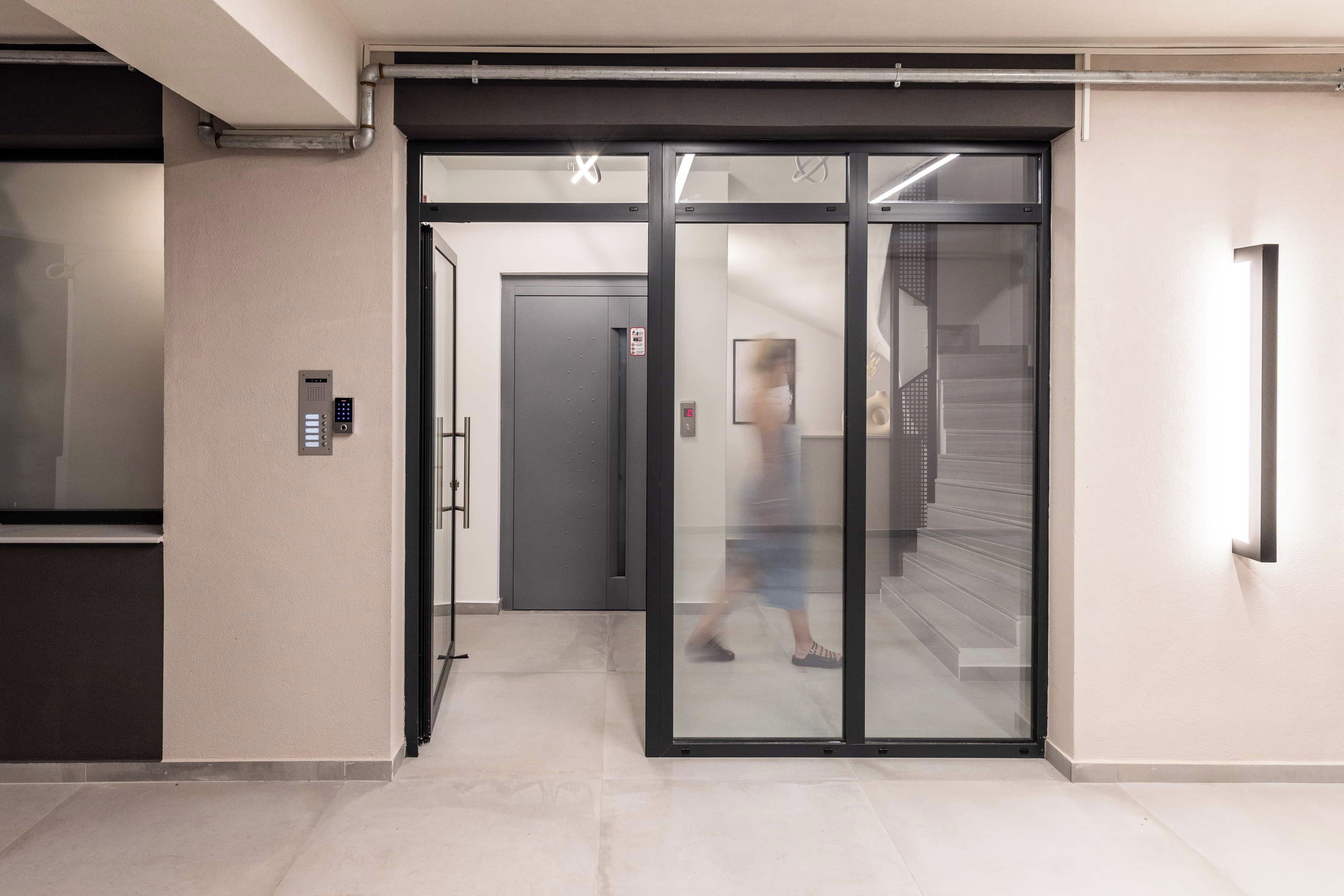 A modern elevator with a digital control panel, a glass door, and a staircase leading to another floor.