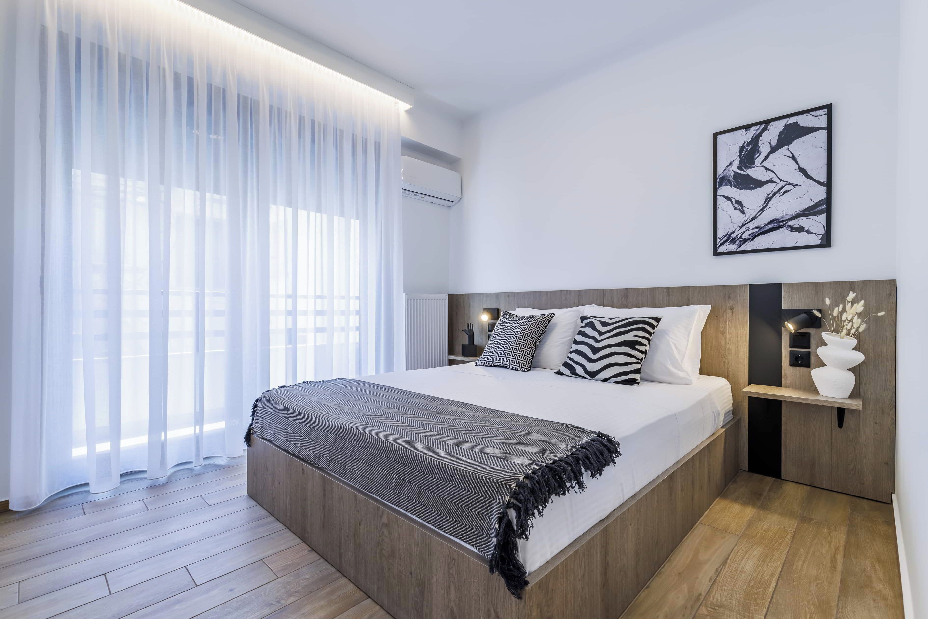 A modern bedroom with a large bed, a bedside table with a lamp, and a wall-mounted artwork.
