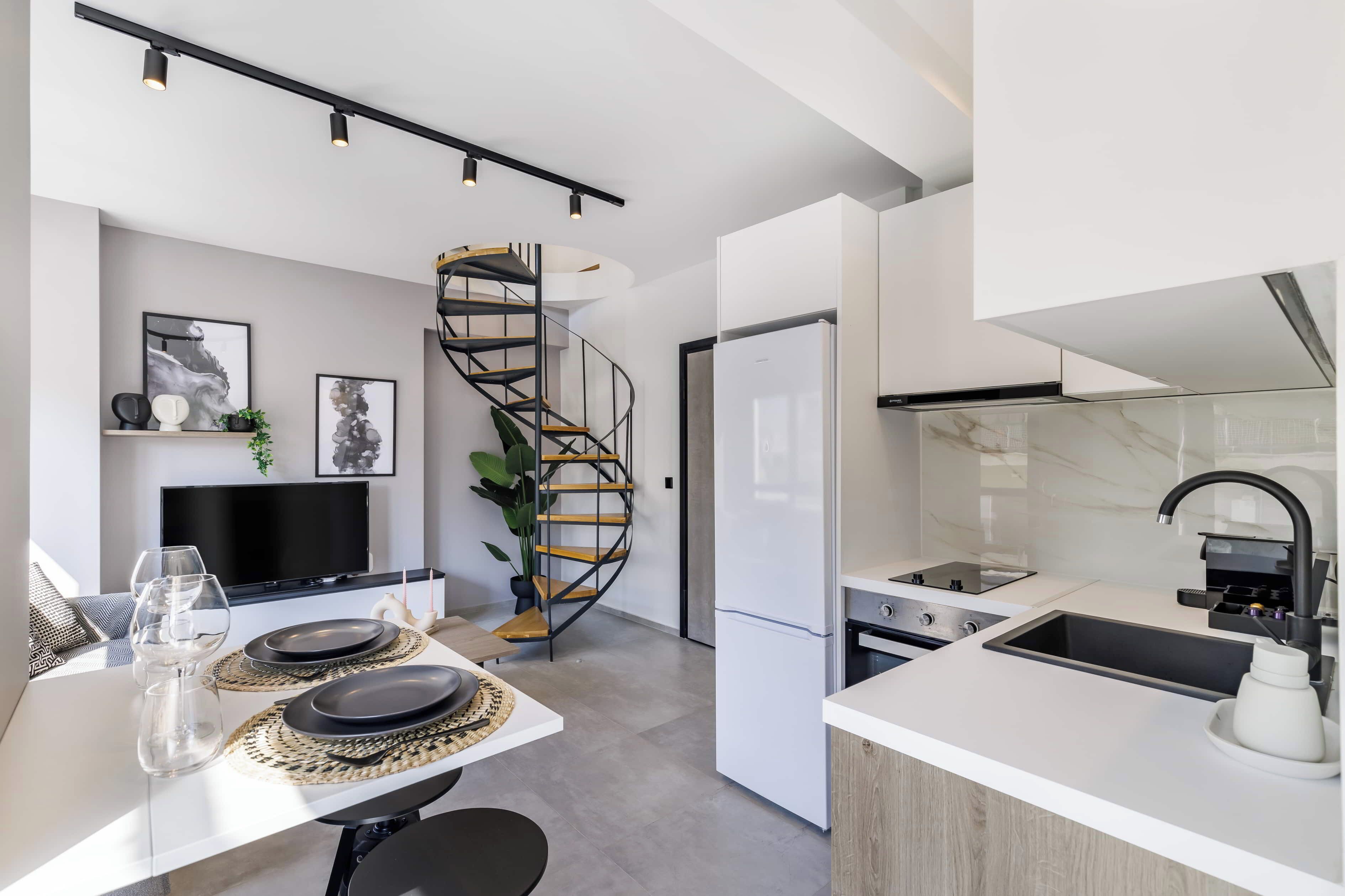 A modern kitchen with a built-in stove, a sink, and a spiral staircase leading to an upper level.