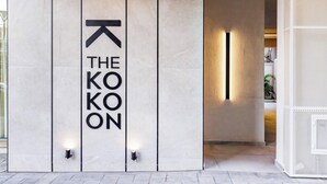 A hotel entrance with a modern design, featuring a vertical sign with the name "THE KOKON" and a directional arrow. - The Kokoon Volos Comfort Living (Volos)