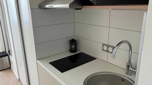 Eine kompakte Küche mit Spüle aus Edelstahl, einer schwarzen Induktionskochplatte, einer eingebauten Mikrowelle und einer Edelstahl-Dunstabzugshaube.