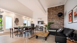 Amplia sala de estar con una mesa de comedor, un sofá de cuero negro y una pared de ladrillo decorativa.