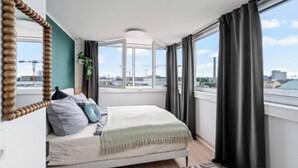 Un dormitorio con cama, un espejo grande, una ventana con cortinas y vistas a la ciudad.