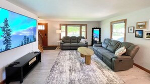 A living room with a large flat-screen TV, two gray sofas, a wooden coffee table, and a patterned rug. - Great Location close to Resch/Lambeau, Sleeps 14, Huge Game Room, Private Yard (Green Bay)