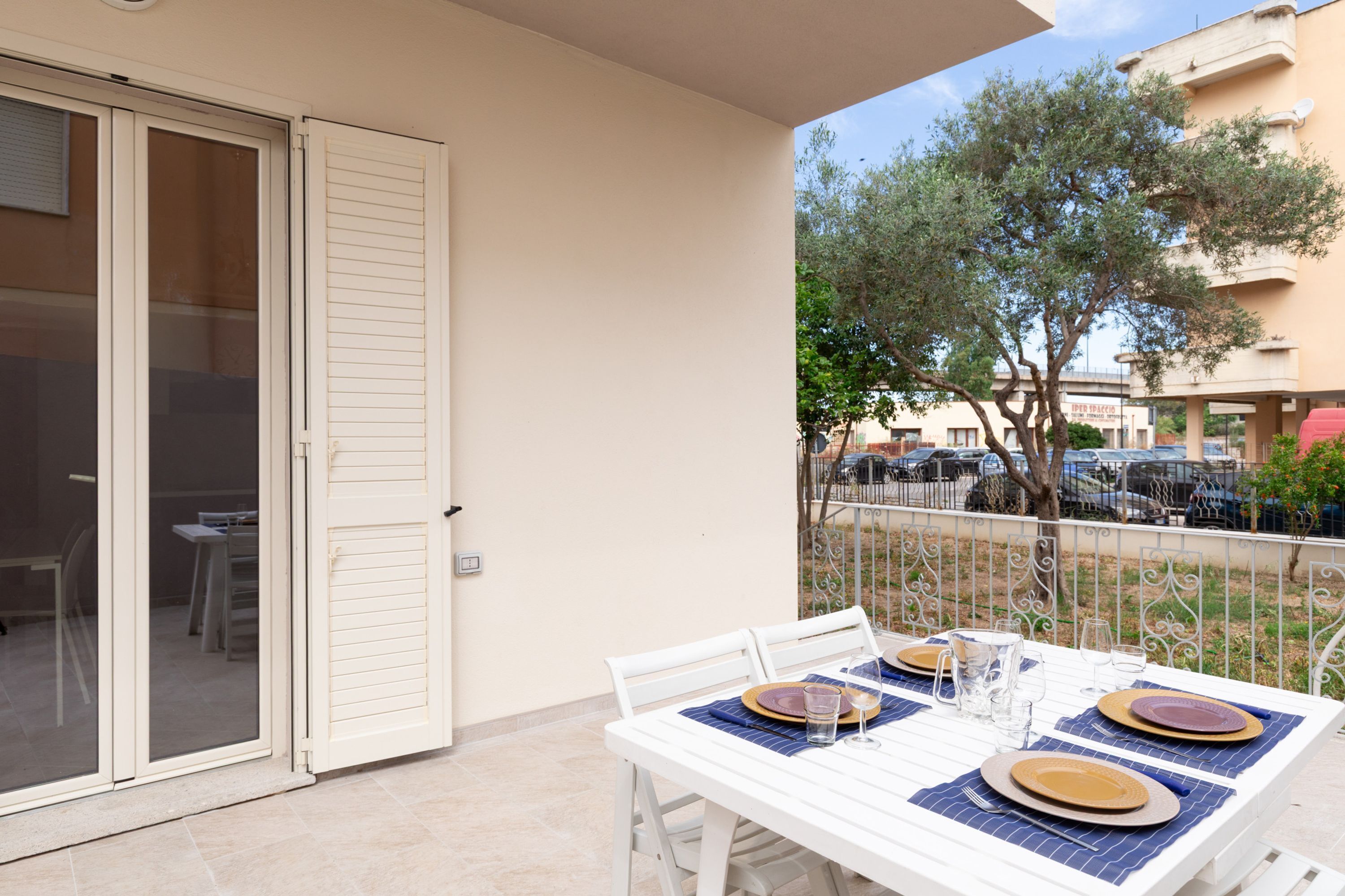 Un balcon avec une table dressée pour quatre personnes, une porte-fenêtre coulissante et une vue sur les voitures garées et les arbres.