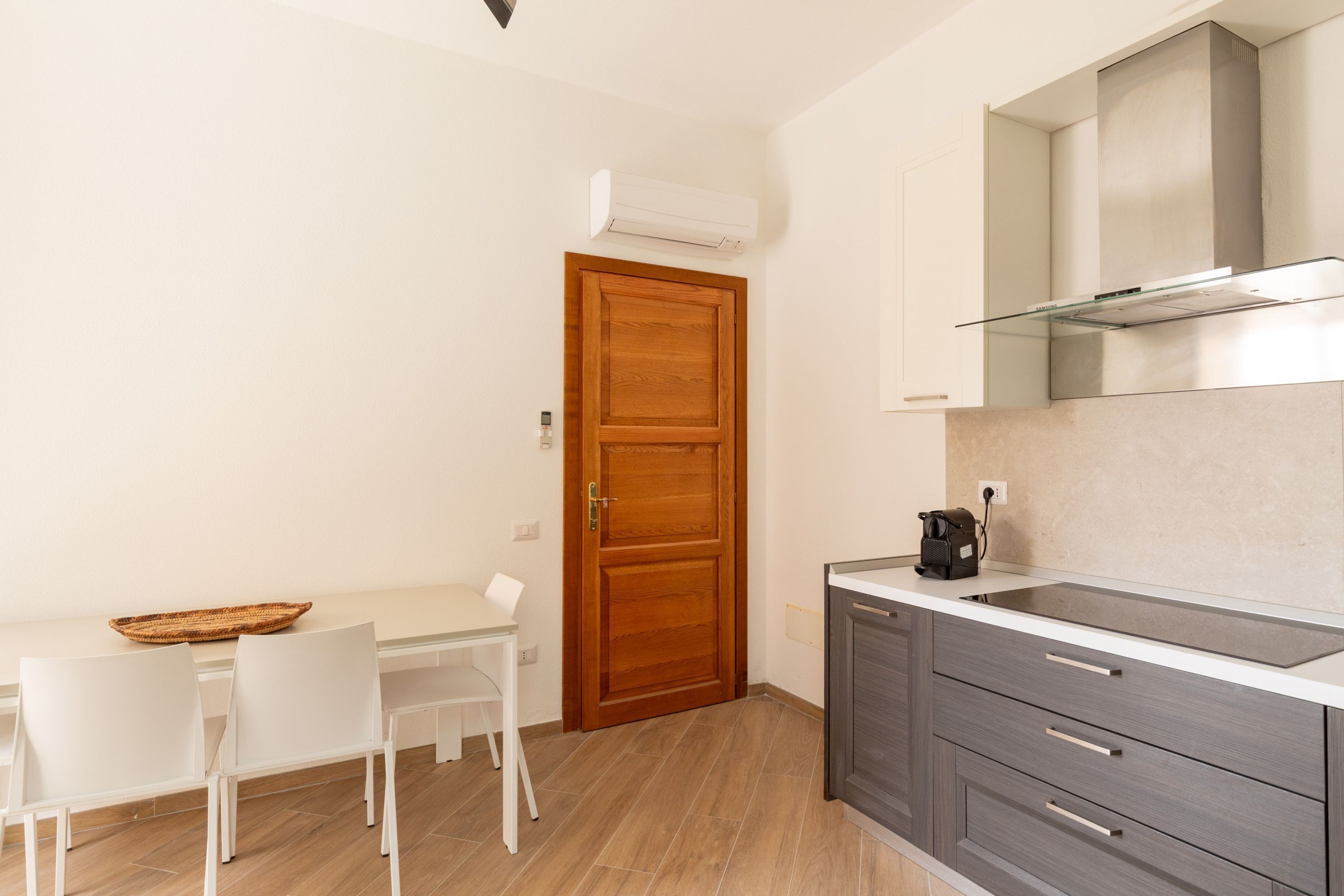 A compact kitchen with a wooden door, white chairs, a small dining table, and a modern stove.