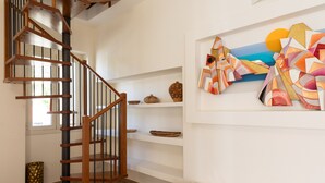 A spiral staircase with wooden railings and a black handrail, leading to a landing with a white wall and a colorful abstract painting. - Casa Marina con Patio by Wonderful Italy (Olbia)