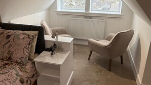 A small, modern bedroom with a sloped ceiling, a large window, a bed, a desk, and a chair.
