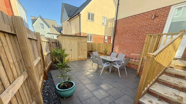 A patio area with a table and chairs, a potted plant, and a wooden fence.