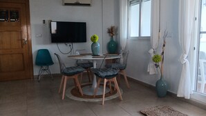 Un coin repas comprenant une table ronde, quatre chaises, un téléviseur à écran plat fixé au mur et une fenêtre avec des rideaux.