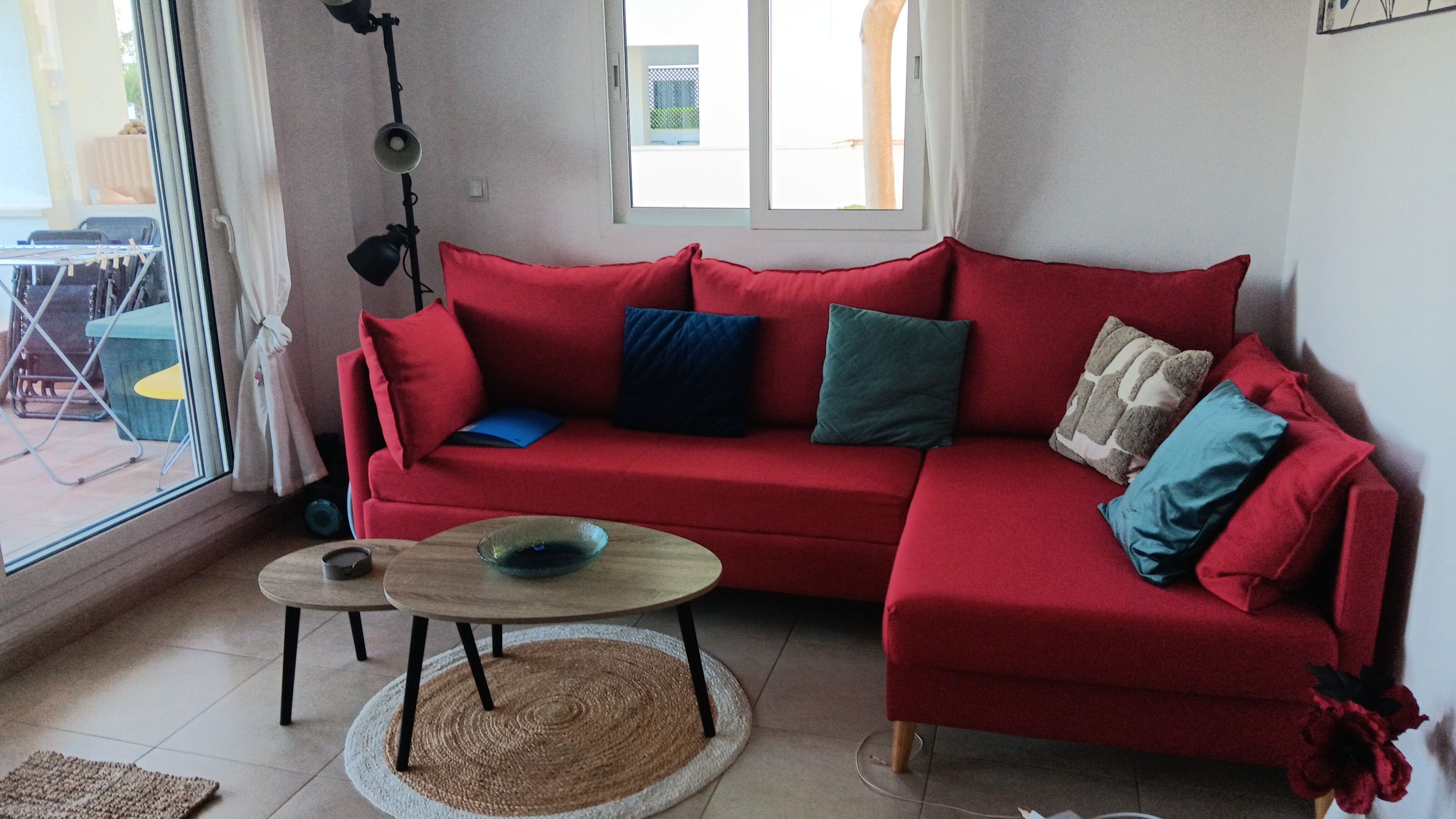 A red sofa with multiple cushions, a small round table with a bowl, and a floor lamp.