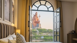 Ett hotellrum med en stor säng, utsikt över en staty genom en öppen dörr och en takfläkt.