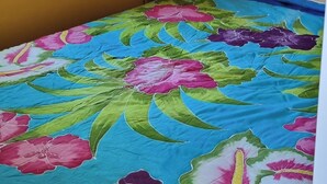 Una cama individual con colcha estampada, cabecera de madera, mesita de noche pequeña y ventana con cortinas.
