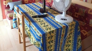 Una habitación con una mesa de madera, un ventilador, un sofá y una estantería con objetos.