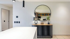 A modern bedroom with a large bed, a bedside table with a mirror, and a small console table with a lamp and decorative items.