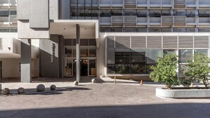 A modern building with a glass facade, a covered entrance, and a landscaped area with spherical stones and a small tree.