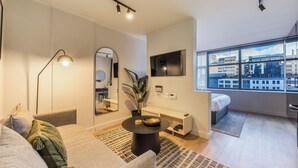 Een moderne woonkamer met een bank, een salontafel, een televisie en een groot raam met uitzicht op de stad.
