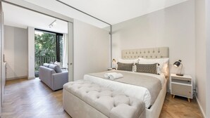 A modern bedroom with a large bed, a sofa, and a view of greenery outside.