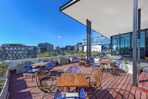 Une terrasse sur le toit, avec des tables en bois et des chaises bleues, d’où l’on peut admirer la vue sur la ville.