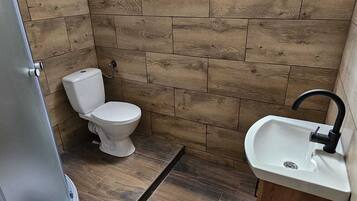 A small bathroom with wooden wall tiles, a toilet, a sink, and a skylight.