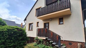 A two-story house with a balcony, a small front porch, and a paved driveway. - Apartmány ŠTĚSTÍ (Bechlin)