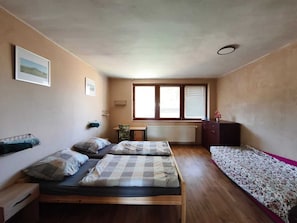 A small room with two beds, a desk, a radiator, and a window with blinds. - Apartmány ŠTĚSTÍ (Bechlin)